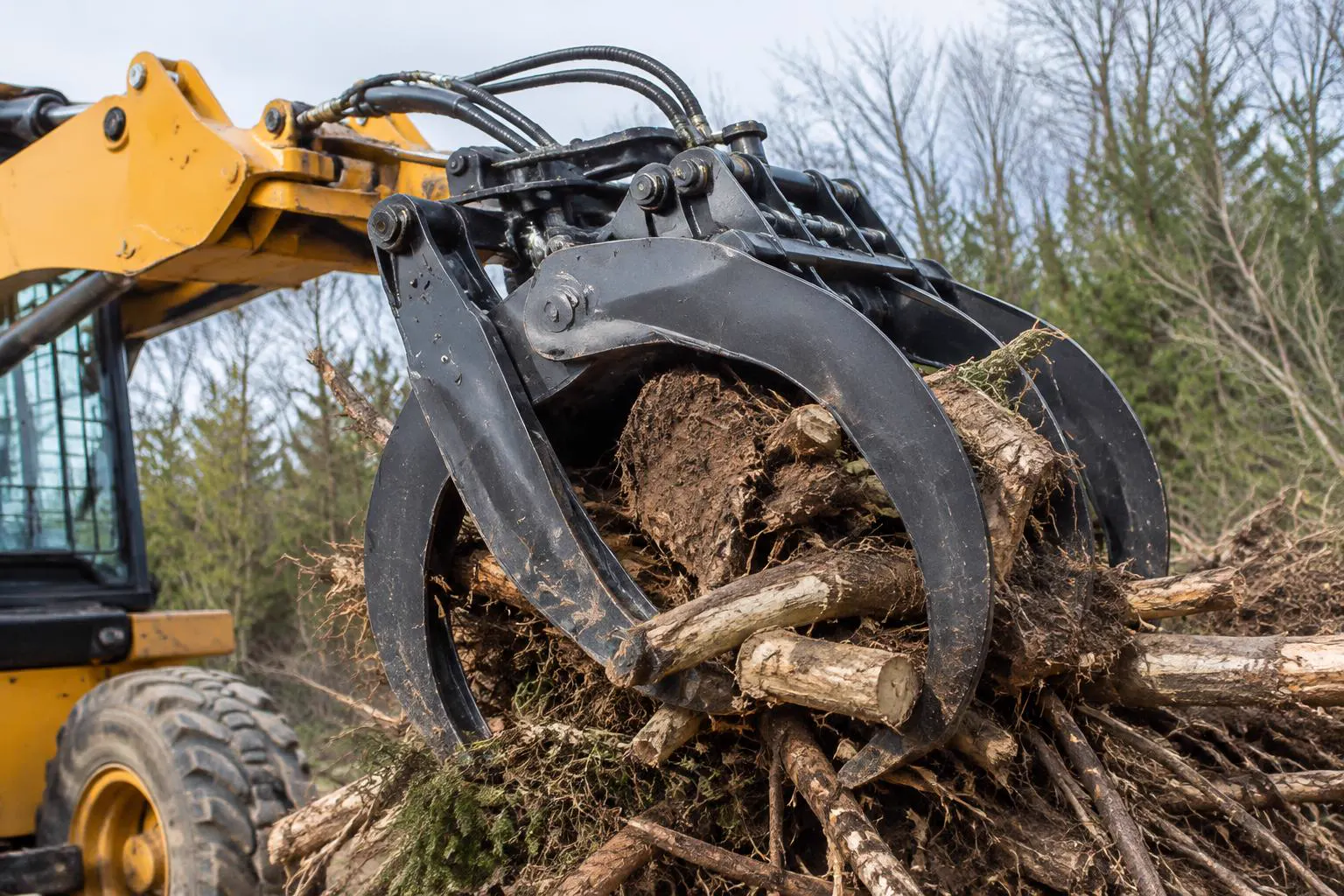 Root grapple attachment on a loader gripping logs and brush